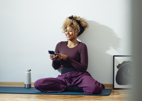 Lady sitting on yoga mat using her phone