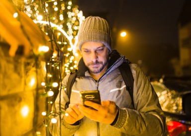 Man dressed warmly checking his phone surrounded by fairy lights