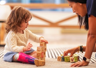 Early years childcare staff member plays blocks with toddler girl