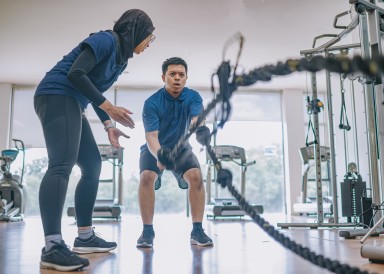 Asian female personal trainer coaching man on ropes